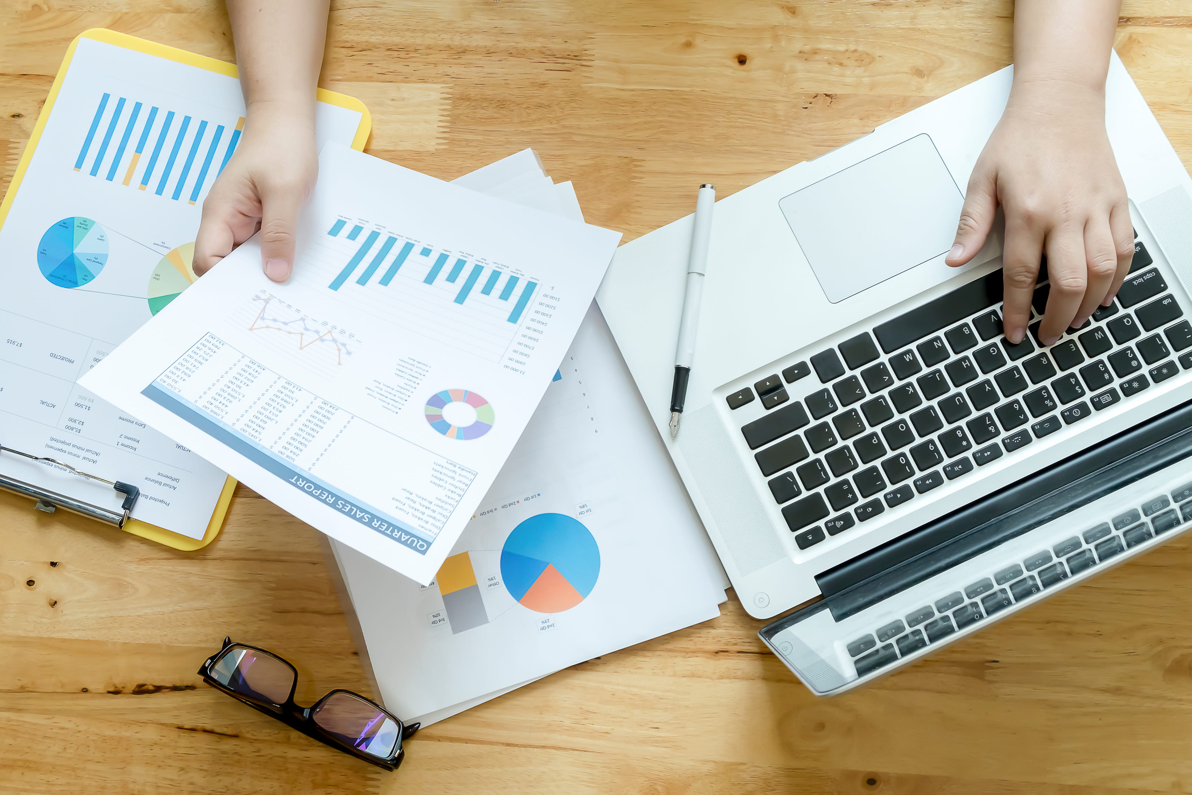 Topview of office desk with documents and laptop, with a woman viewing the results from various survey data collection methods